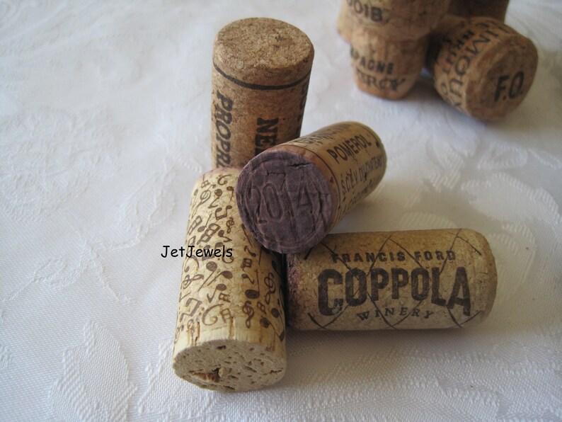 May include: A collection of used wine corks. One cork has musical notes, another has the year "2014" stamped on it. The corks are made of natural cork material and feature various winery names and designs.