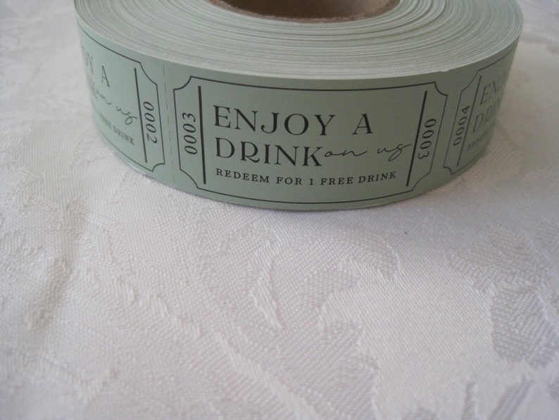 Puede incluir: Un rollo de tickets de papel verde con texto negro que dice "Disfruta de una bebida por nuestra cuenta. Canjea por 1 bebida gratis." Los tickets est&aacute;n numerados 00003.