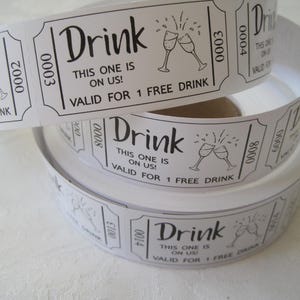 Op de afbeelding: Een rol witte papieren dranktickets met zwarte tekst en een afbeelding van twee champagne glazen. De tekst luidt "Drink This one is on us! Valid for 1 free drink".