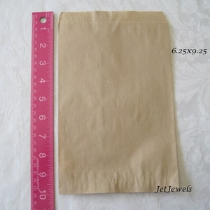 May include: A brown paper bag with a 6.25 x 9.25 inch measurement. The bag is folded and has a crease down the middle.