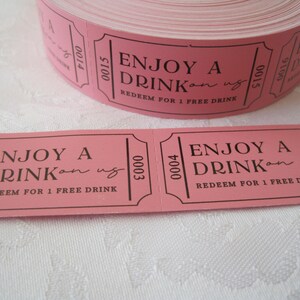 Op de afbeelding: Roze papieren tickets met zwarte tekst die "Geniet van een drankje op ons" en "Inwisselen voor 1 gratis drankje" luidt.
