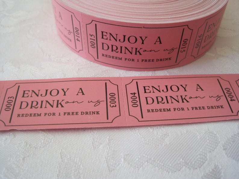 Op de afbeelding: Roze papieren tickets met zwarte tekst die "Geniet van een drankje op ons" en "Inwisselen voor 1 gratis drankje" luidt.