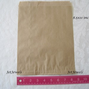 May include: A brown paper bag measuring 8.5 by 11 inches. The bag is lying flat on a white surface with a pink ruler underneath.