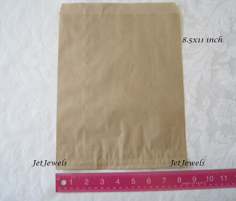 May include: A brown paper bag measuring 8.5 by 11 inches. The bag is lying flat on a white surface with a pink ruler underneath.