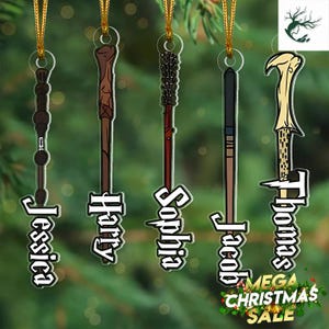May include: Five decorative wand ornaments with gold hanging strings. Each wand is a different color and design, with names like "Jessica", "Harry", "Sophia", "Jacob", and "Thomas" in white text. The background is a blurred green.