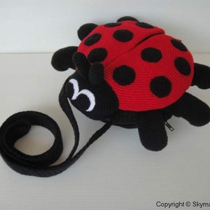 May include: A red and black crocheted ladybug purse with a black strap. The purse has a zipper closure and white eyes.