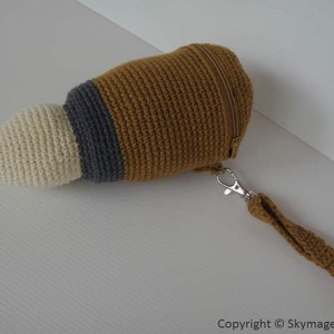 May include: A crocheted pouch with a zipper closure and a brown, white, and gray color scheme. The pouch has a brown strap with a silver clasp.