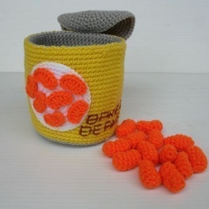 K&ouml;nnte beinhalten: Eine geh&auml;kelte gelbe Dose mit einem grauen Deckel, gef&uuml;llt mit orangefarbenen geh&auml;kelten Bohnen. Die Dose tr&auml;gt den Text "BAKED BEANS" an der Seite.