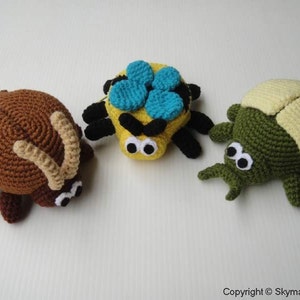 May include: Three crocheted stuffed bugs. A brown beetle with tan horns, a yellow and black spider with blue wings, and a green beetle with a yellow shell.