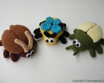 May include: Three crocheted stuffed bugs. A brown beetle with tan horns, a yellow and black spider with blue wings, and a green beetle with a yellow shell.