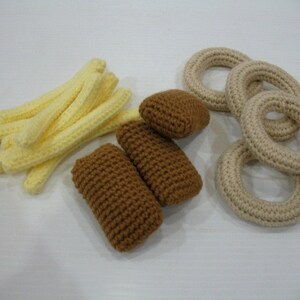 May include: A set of crocheted food items, including french fries, onion rings, and fish sticks. The fries are yellow, the onion rings are beige, and the fish sticks are brown.
