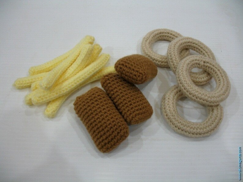 May include: A set of crocheted food items, including french fries, onion rings, and fish sticks. The fries are yellow, the onion rings are beige, and the fish sticks are brown.