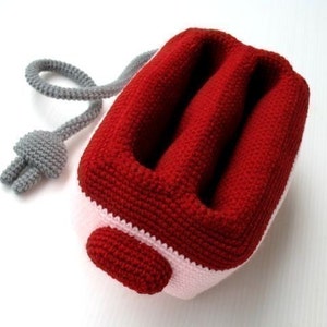 May include: A red and white crocheted plush toy shaped like a toaster. The toaster has a gray cord.