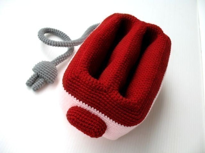 May include: A red and white crocheted plush toy shaped like a toaster. The toaster has a gray cord.