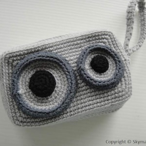 May include: Gray crocheted pouch with a zipper closure and a handle. The pouch has two large gray and black eyes.