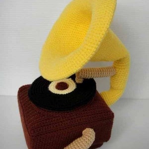 May include: A crocheted plush toy shaped like a vintage record player. The record player is brown with a black record and a yellow horn.