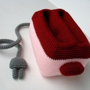 May include: A crocheted toaster with a pink and red color scheme. The toaster has a gray crocheted cord.
