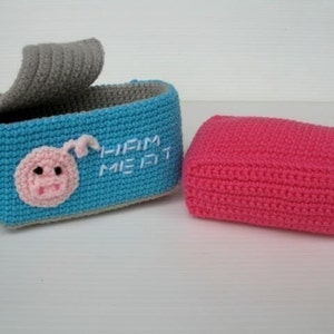K&ouml;nnte beinhalten: Eine blaue geh&auml;kelte Box mit einem grauen Deckel und einem gestickten rosa Schweinegesicht auf der Vorderseite. Die Box tr&auml;gt die Aufschrift "Liam Meet" in wei&szlig;er Stickerei. Daneben befindet sich eine rosa geh&auml;kelte Box.