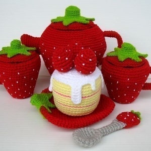 May include: A red crocheted strawberry tea set with a teapot, two cups, a sugar bowl, a cake, and a spoon. The set is perfect for pretend play.