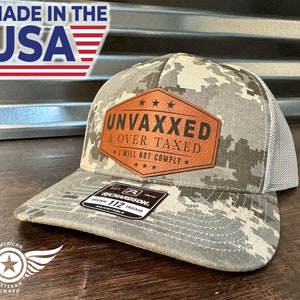 Peut inclure: Un chapeau de camionneur camouflage avec un patch en cuir marron qui dit "UNVAXXED & OVER TAXED I WILL NOT COMPLY" avec trois étoiles au-dessus et en dessous du texte. Le chapeau est fabriqué par Richardson et est réglable.