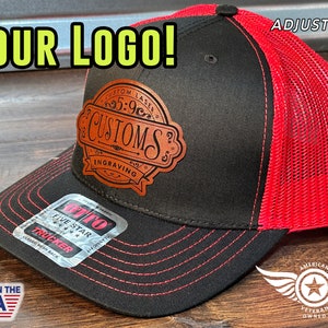 May include: A black and red trucker hat with a brown leather patch that says "Custom Laser 5:9c Customs Engraving". The hat is adjustable and has a mesh back. The hat also has a tag that says "Otto Five Star Trucker Classic Mesh Back".