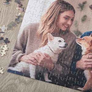 May include: A couple are holding their two dogs. The woman is wearing a brown sweater and the man is wearing a blue shirt. The dogs are a white dog and a brown and white dog.