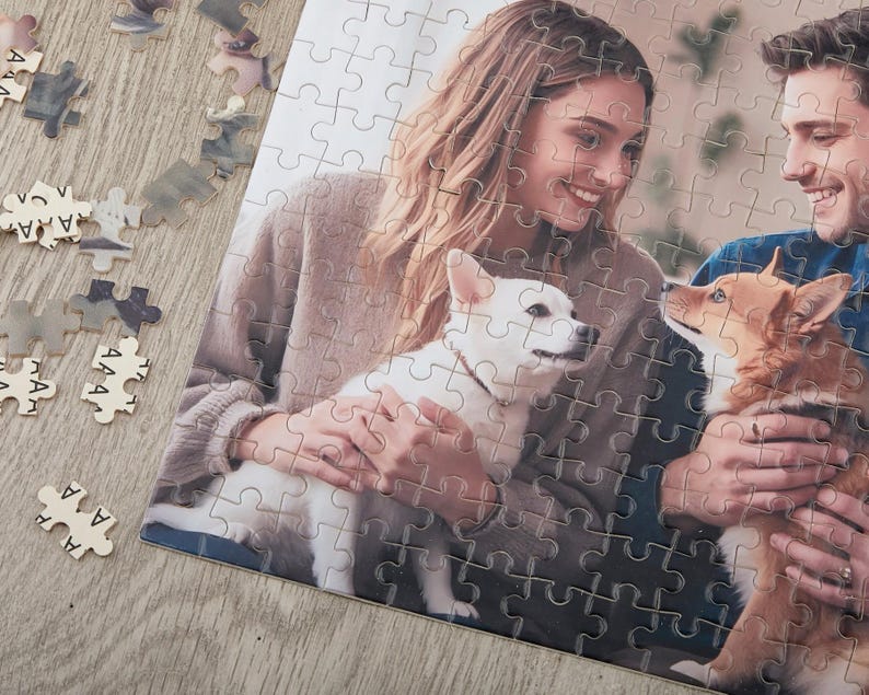 May include: A couple are holding their two dogs. The woman is wearing a brown sweater and the man is wearing a blue shirt. The dogs are a white dog and a brown and white dog.