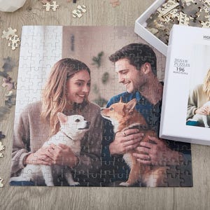 May include: A 196 piece jigsaw puzzle featuring a couple with their two dogs. The puzzle is made of high quality wood and comes in a white box with the words "Jigsaw Puzzles 196" printed on it.