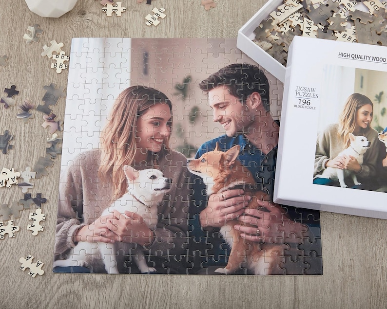 May include: A 196 piece jigsaw puzzle featuring a couple with their two dogs. The puzzle is made of high quality wood and comes in a white box with the words "Jigsaw Puzzles 196" printed on it.