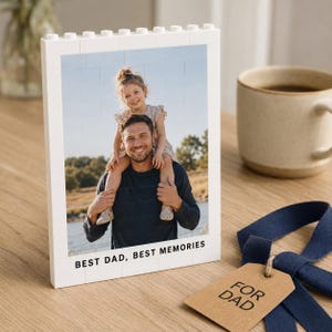 Könnte beinhalten: Ein weißer, rechteckiger Bilderrahmen aus Bausteinen mit einem Foto eines Kindes, das auf den Schultern einer Person sitzt. Der Rahmen enthält am unteren Rand den aufgedruckten Text BEST DAD, BEST MEMORIES.