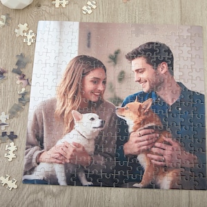 May include: A couple pose with their two dogs in a jigsaw puzzle. The puzzle features a close-up of the couple and their dogs, with a blurred background.