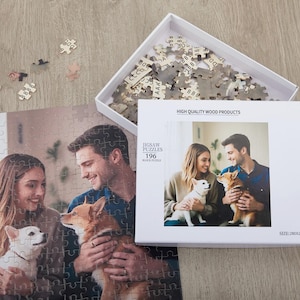 May include: A white box with a photo of a couple and their two dogs on the front. The box contains a 196 piece jigsaw puzzle. The text on the box reads "Jigsaw Puzzles 196 Block Puzzle" and "High Quality Wood Products".