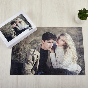 May include: A 300-piece jigsaw puzzle featuring a couple posing together in a woodland setting. The puzzle is made of cardboard and has a matt finish.