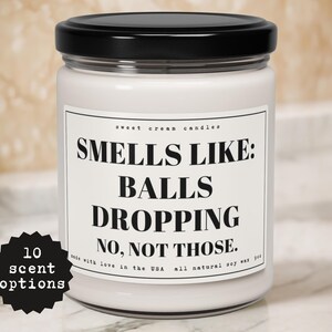 May include: White candle jar with a black lid and a white label that reads "Smells Like: Balls Dropping No, Not Those." Made with love in the USA. All natural soy wax.