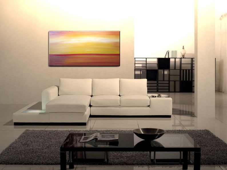 May include: A white sectional sofa with a low coffee table in front of it. The sofa is in a modern living room with a large abstract painting on the wall behind it.