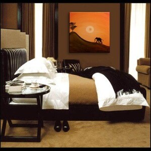 May include: A bedroom with a bed with white linens and a black throw blanket. The bed is next to a small black side table. There is a painting on the wall of a silhouette of an elephant walking on a hill with a tree and a sun in the background.
