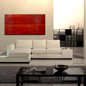 K&ouml;nnte beinhalten: Ein wei&szlig;es Ecksofa mit einem roten abstrakten Gem&auml;lde an der Wand dahinter. Das Sofa hat eine Chaiselongue auf der linken Seite und einen Couchtisch davor.