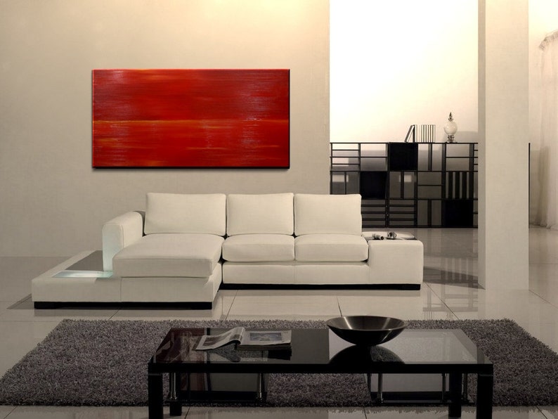 K&ouml;nnte beinhalten: Ein wei&szlig;es Ecksofa mit einem roten abstrakten Gem&auml;lde an der Wand dahinter. Das Sofa hat eine Chaiselongue auf der linken Seite und einen Couchtisch davor.