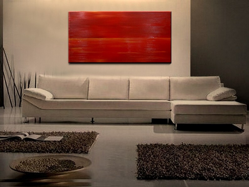 K&ouml;nnte beinhalten: Abstraktes Gem&auml;lde mit horizontalen Pinselstrichen in Rot- und Oranget&ouml;nen. Das Gem&auml;lde h&auml;ngt an einer Wand &uuml;ber einem wei&szlig;en Ecksofa.
