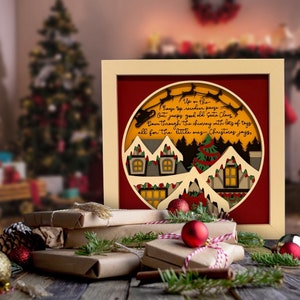 May include: A framed 3D paper art piece with a red background and a yellow circle in the center. The circle depicts a snowy winter scene with houses, trees, and a reindeer pulling a sleigh. The text "Up on the house top reindeer pause. Out jumps good old Santa Claus Down through the chimney with lots of toys all for the little ones Christmas joys" is written in black on the yellow circle.