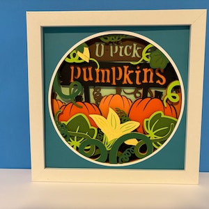 May include: A framed paper craft with a round cutout featuring a sign that says "U-pick pumpkins" and a 3D paper design of pumpkins, leaves, and vines.