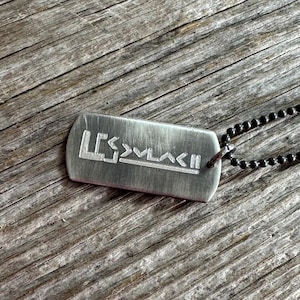 May include: A silver dog tag necklace with a black chain. The dog tag has the word "LESS" engraved on it, followed by a series of arrows.