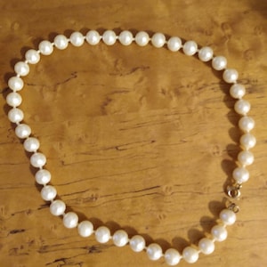 May include: A classic pearl necklace featuring round, off-white pearls strung together. The necklace is secured with a gold-colored clasp. The pearls are evenly spaced, creating a timeless and elegant look.