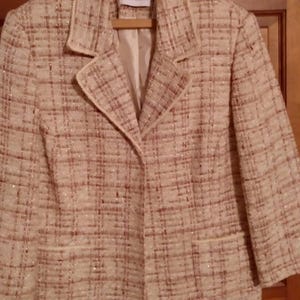 May include: A beige and cream tweed blazer featuring a textured plaid pattern with subtle metallic threading, a notched lapel, long sleeves, two front pockets, and a button closure. The interior label reads Alfred Dunner.
