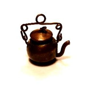 May include: A miniature dark brown metal teapot featuring a rounded body, a small lid with a central knob, and a curved spout. The teapot includes a decorative wire handle with curled ends and a circular loop at the top for hanging or attachment.