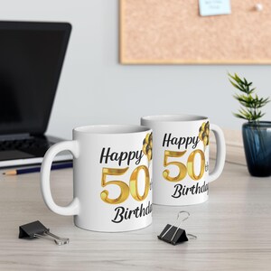 May include: Two white ceramic mugs with black text and gold numbers. The mugs say "Happy 50th Birthday".