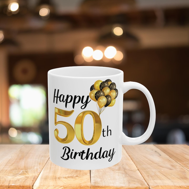 May include: White ceramic mug with a black and gold design. The mug says "Happy 50th Birthday" with gold balloons.