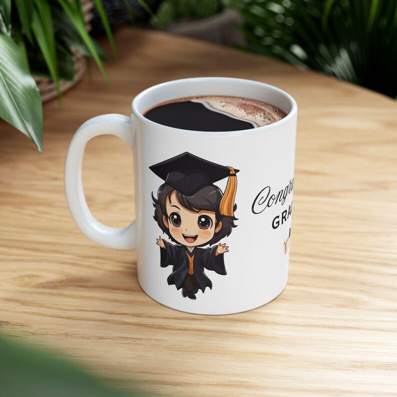 May include: White ceramic coffee mug with a black handle. The mug features a cartoon illustration of a graduate wearing a black cap and gown. The text "Congrats Grad" is printed on the mug.