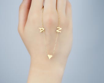 Op de afbeelding: Een gouden ketting met een hartvormige hanger en twee hangers met initialen. De initialen zijn "A" en "N".