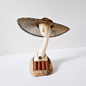 May include: A ceramic ring holder shaped like a woman's head wearing a wide-brimmed straw hat with a brown and black leopard print base.